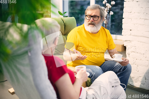 Image of Couple of seniors spending time together being quarantined - caucasians mature and retired man and woman using modern gadgets, talking, drinking tea