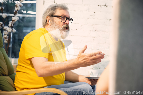 Image of Couple of seniors spending time together being quarantined - caucasians mature and retired man and woman using modern gadgets, talking, drinking tea