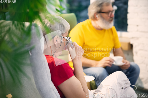 Image of Couple of seniors spending time together being quarantined - caucasians mature and retired man and woman using modern gadgets, talking, drinking tea