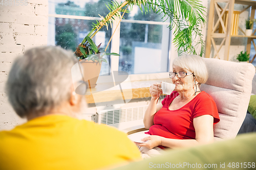 Image of Couple of seniors spending time together being quarantined - caucasians mature and retired man and woman using modern gadgets, talking, drinking tea