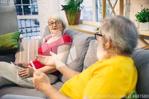 Image of Couple of seniors spending time together being quarantined - caucasians mature and retired man and woman using modern gadgets, talking, drinking tea