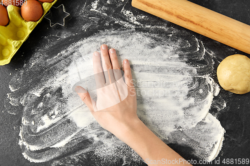 Image of hand with flour, dough and rolling pin on table