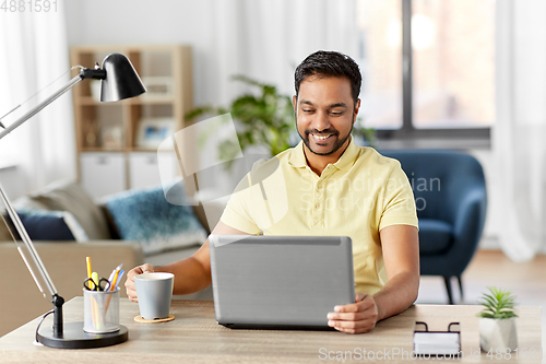 Image of man with laptop drinking coffee at home office