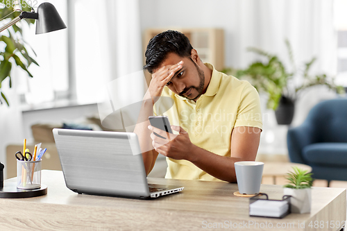 Image of happy indian man with smartphone at home office