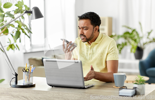 Image of man recording voice on smartphone at home office