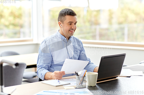 Image of man in earphones with laptop working at home