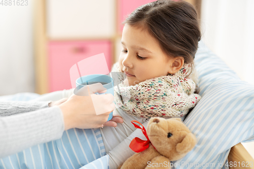 Image of mother giving hot tea to sick little daughter