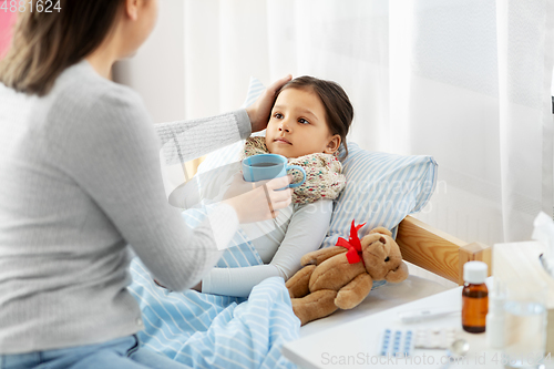 Image of mother giving hot tea to sick little daughter