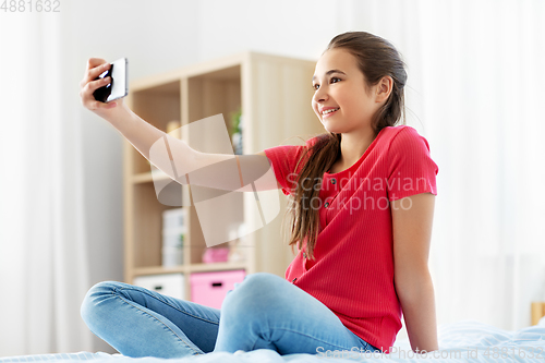 Image of happy girl with smartphone taking selfie at home