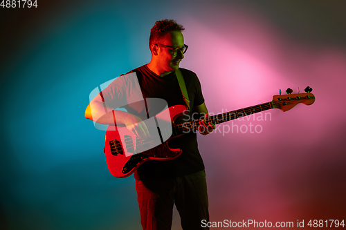 Image of Young caucasian musician playing on gradient background in neon light. Concept of music, hobby, festival