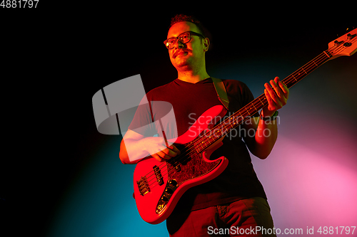 Image of Young caucasian musician playing on gradient background in neon light. Concept of music, hobby, festival