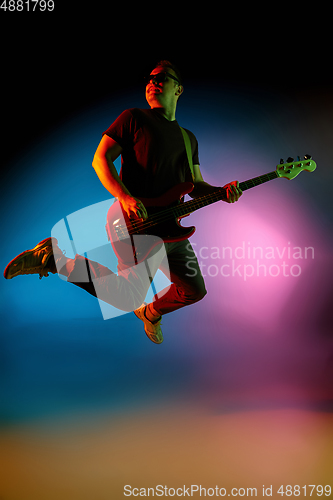 Image of Young caucasian musician playing on gradient background in neon light. Concept of music, hobby, festival