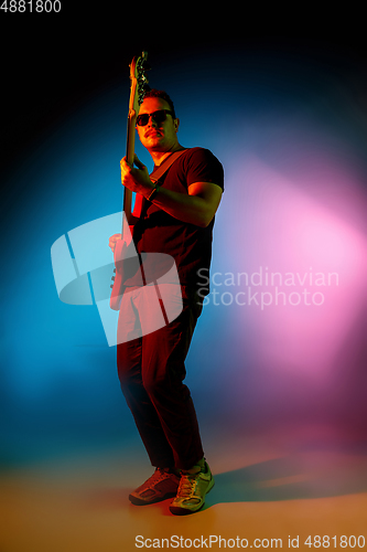 Image of Young caucasian musician playing on gradient background in neon light. Concept of music, hobby, festival