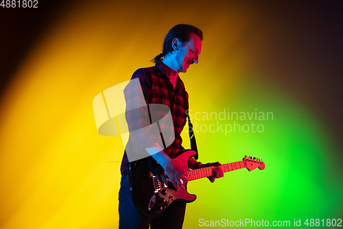 Image of Young caucasian musician playing on gradient background in neon light. Concept of music, hobby, festival