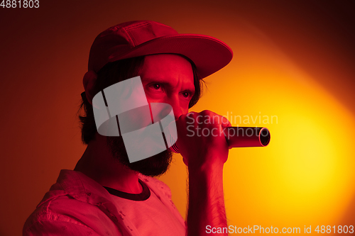 Image of Young caucasian musician playing, singing on gradient background in neon light. Concept of music, hobby, festival