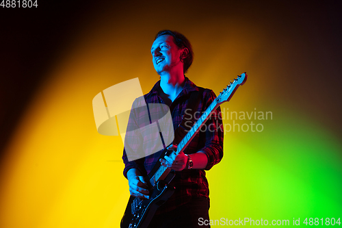 Image of Young caucasian musician playing on gradient background in neon light. Concept of music, hobby, festival