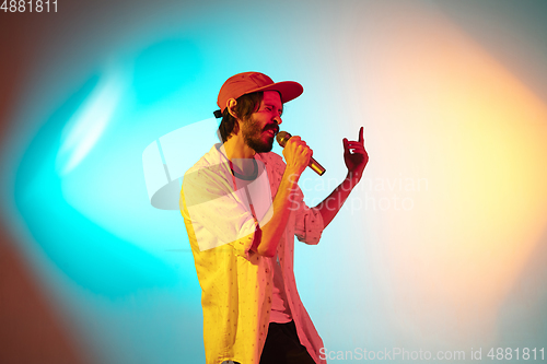 Image of Young caucasian musician playing, singing on gradient background in neon light. Concept of music, hobby, festival