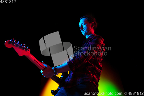 Image of Young caucasian musician playing on gradient background in neon light. Concept of music, hobby, festival