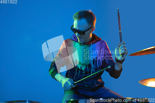 Image of Young caucasian musician playing on gradient background in neon light. Concept of music, hobby, festival