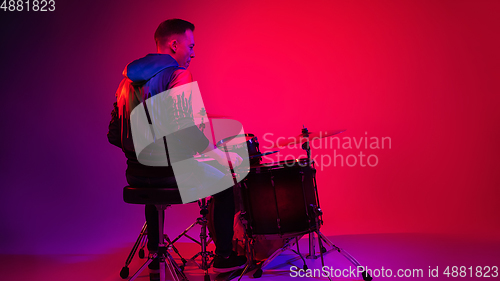 Image of Young caucasian musician playing on gradient background in neon light. Concept of music, hobby, festival