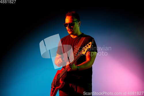 Image of Young caucasian musician playing on gradient background in neon light. Concept of music, hobby, festival