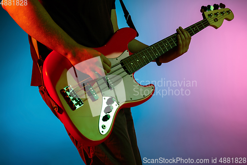 Image of Young caucasian musician playing on gradient background in neon light. Concept of music, hobby, festival