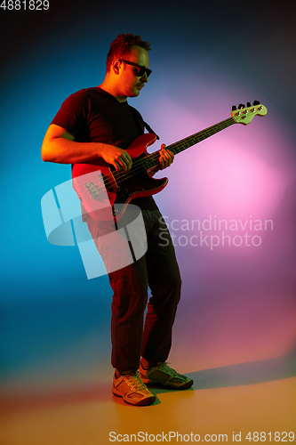 Image of Young caucasian musician playing on gradient background in neon light. Concept of music, hobby, festival