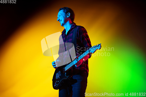 Image of Young caucasian musician playing on gradient background in neon light. Concept of music, hobby, festival