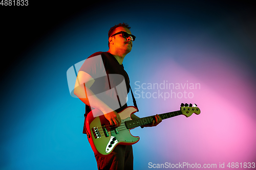 Image of Young caucasian musician playing on gradient background in neon light. Concept of music, hobby, festival