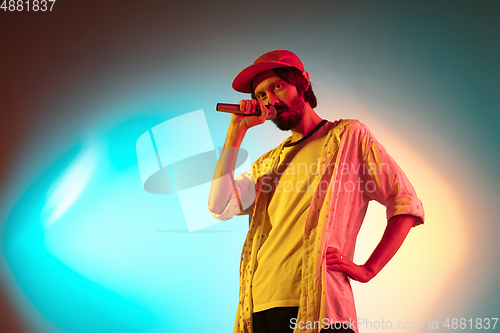 Image of Young caucasian musician playing, singing on gradient background in neon light. Concept of music, hobby, festival