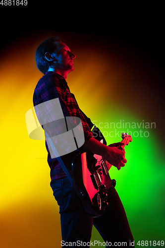 Image of Young caucasian musician playing on gradient background in neon light. Concept of music, hobby, festival