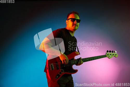 Image of Young caucasian musician playing on gradient background in neon light. Concept of music, hobby, festival