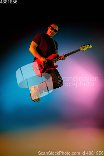 Image of Young caucasian musician playing on gradient background in neon light. Concept of music, hobby, festival