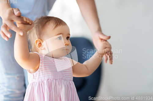 Image of baby girl learning to walk with mother's help