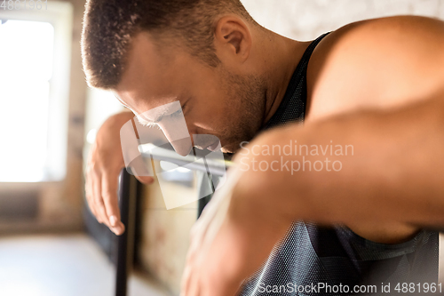 Image of close up of tired man at parallel bars in gym