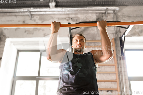 Image of man exercising on bar and doing pull-ups in gym