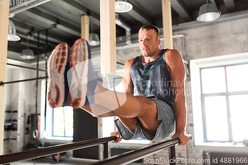 Image of man flexing abs on parallel bars in gym