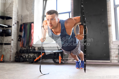 Image of man doing push-ups on gymnastic rings in gym