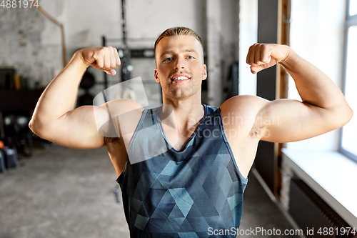 Image of happy young man showing his bicep muscles in gym