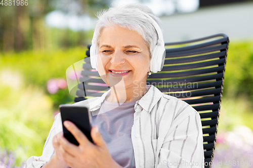 Image of old woman with headphones and smartphone at garden