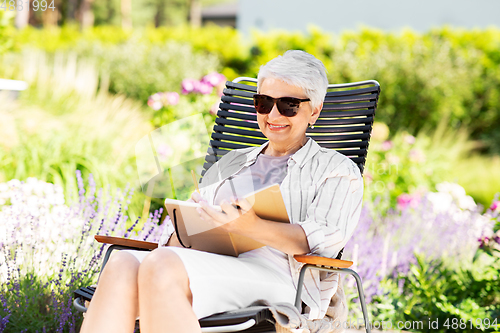 Image of happy senior woman with diary at summer garden