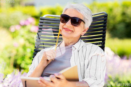 Image of happy senior woman with diary at summer garden