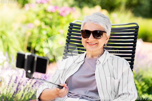 Image of happy senior woman taking selfie at summer garden