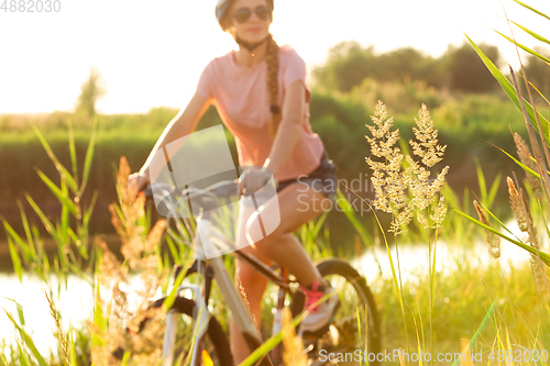 Image of Joyful young woman riding a bicycle at the riverside and meadow promenade