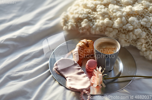 Image of croissant, coffee and eye sleeping mask in bed