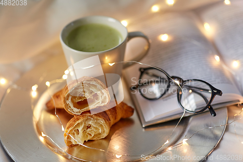 Image of croissants, matcha tea, book and glasses in bed