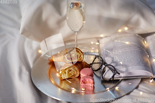 Image of champagne, croissants, book and glasses in bed