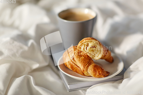 Image of croissants, cup of coffee and book in bed at home