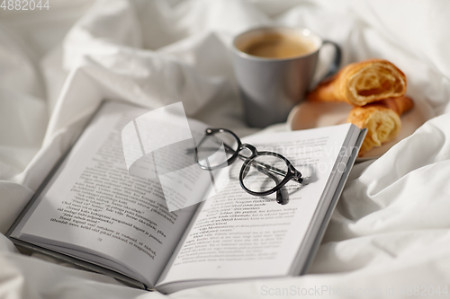 Image of croissants, cup of coffee and book in bed at home