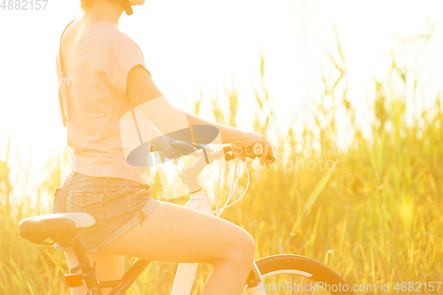 Image of Joyful young woman riding a bicycle at the riverside and meadow promenade